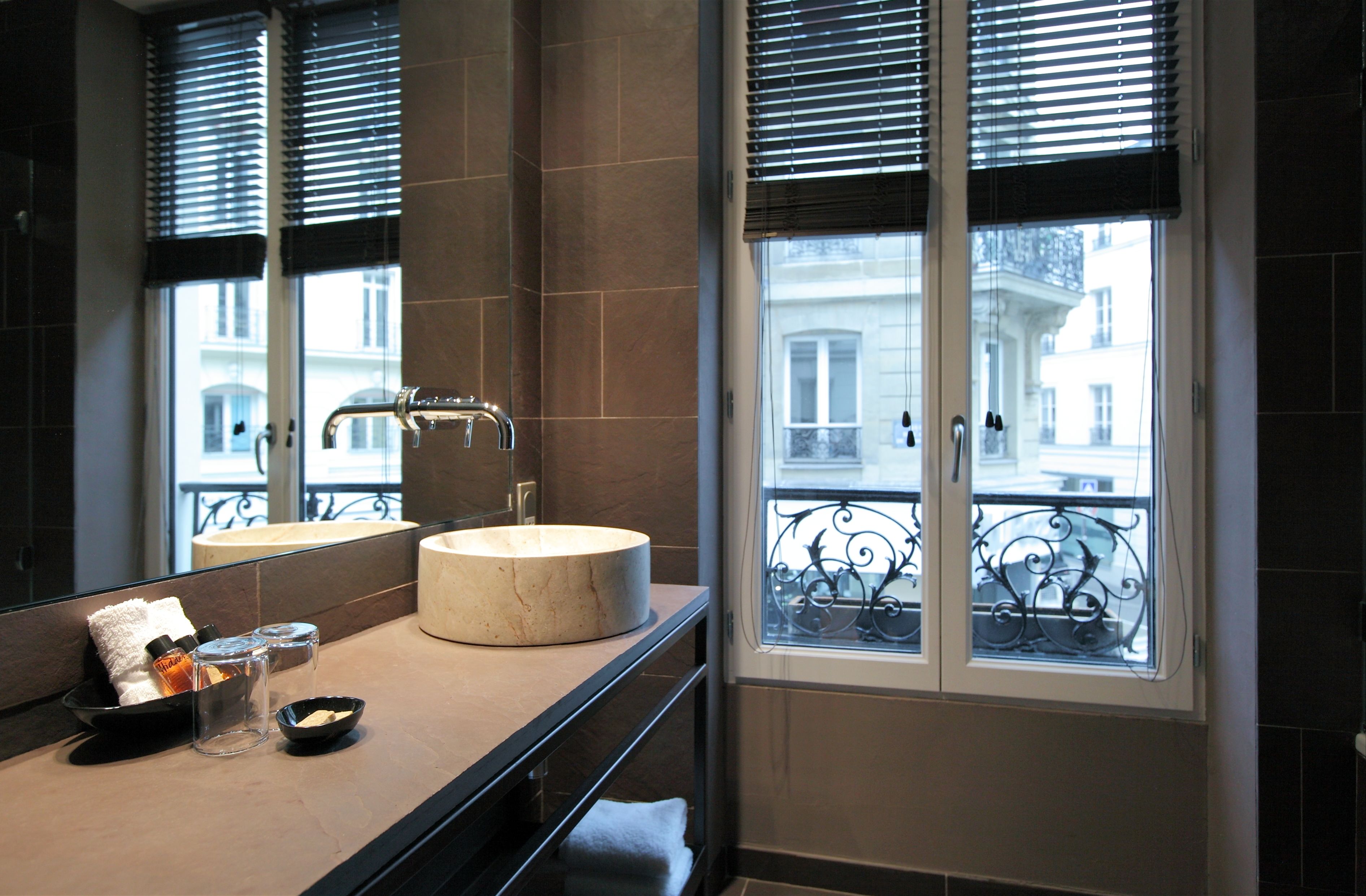 A bathroom with a round sink, a mirror, and a window with a balcony view.