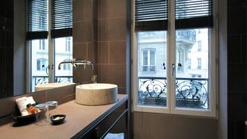 A bathroom with a round sink, a mirror, and a window with a balcony view.