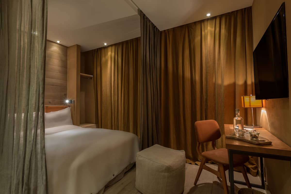 Une chambre d’hôtel avec un lit, un bureau avec une lampe, une chaise et un téléviseur.