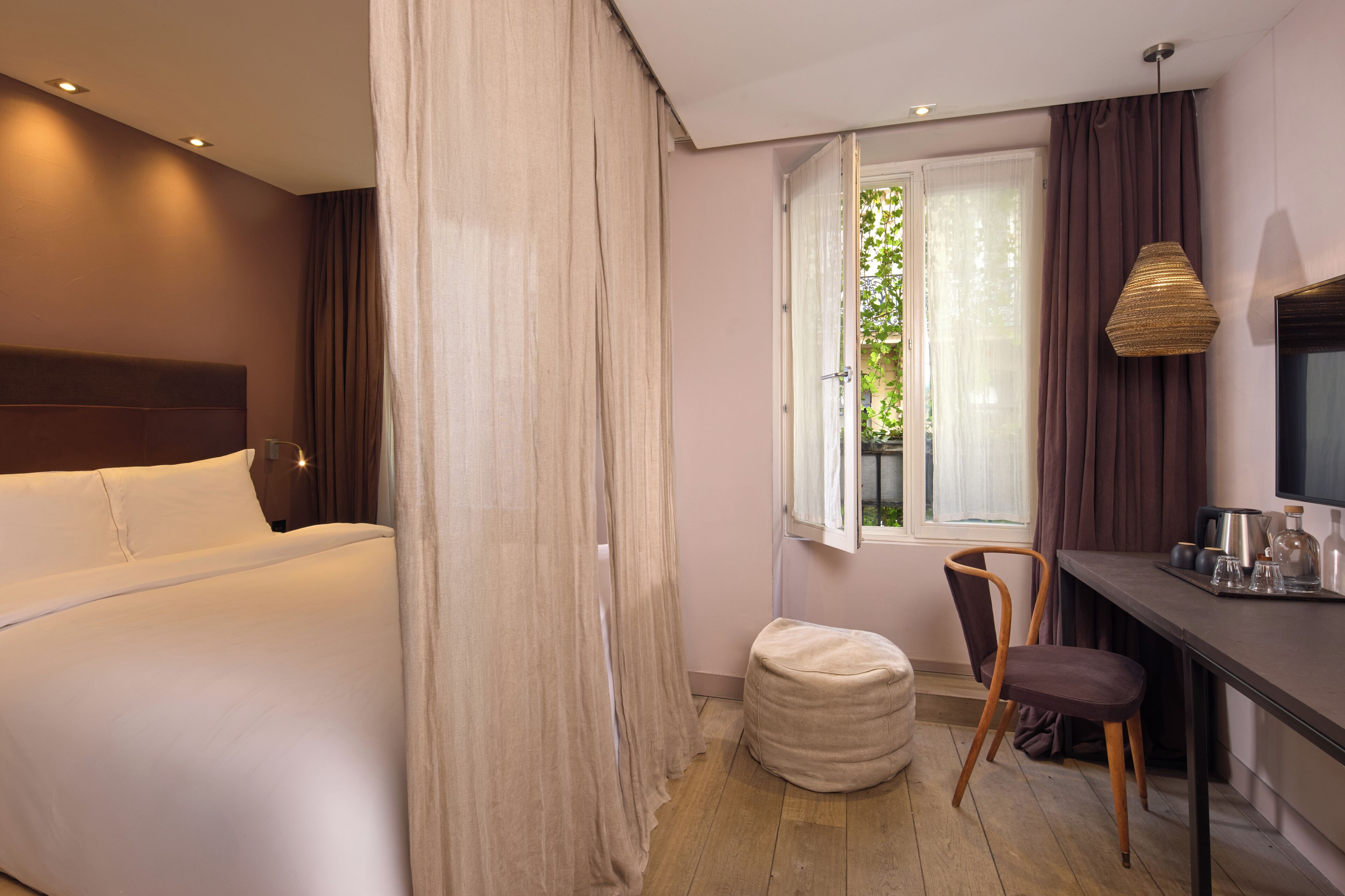 A hotel room with a bed, a desk with a chair, a window with curtains, and a television.