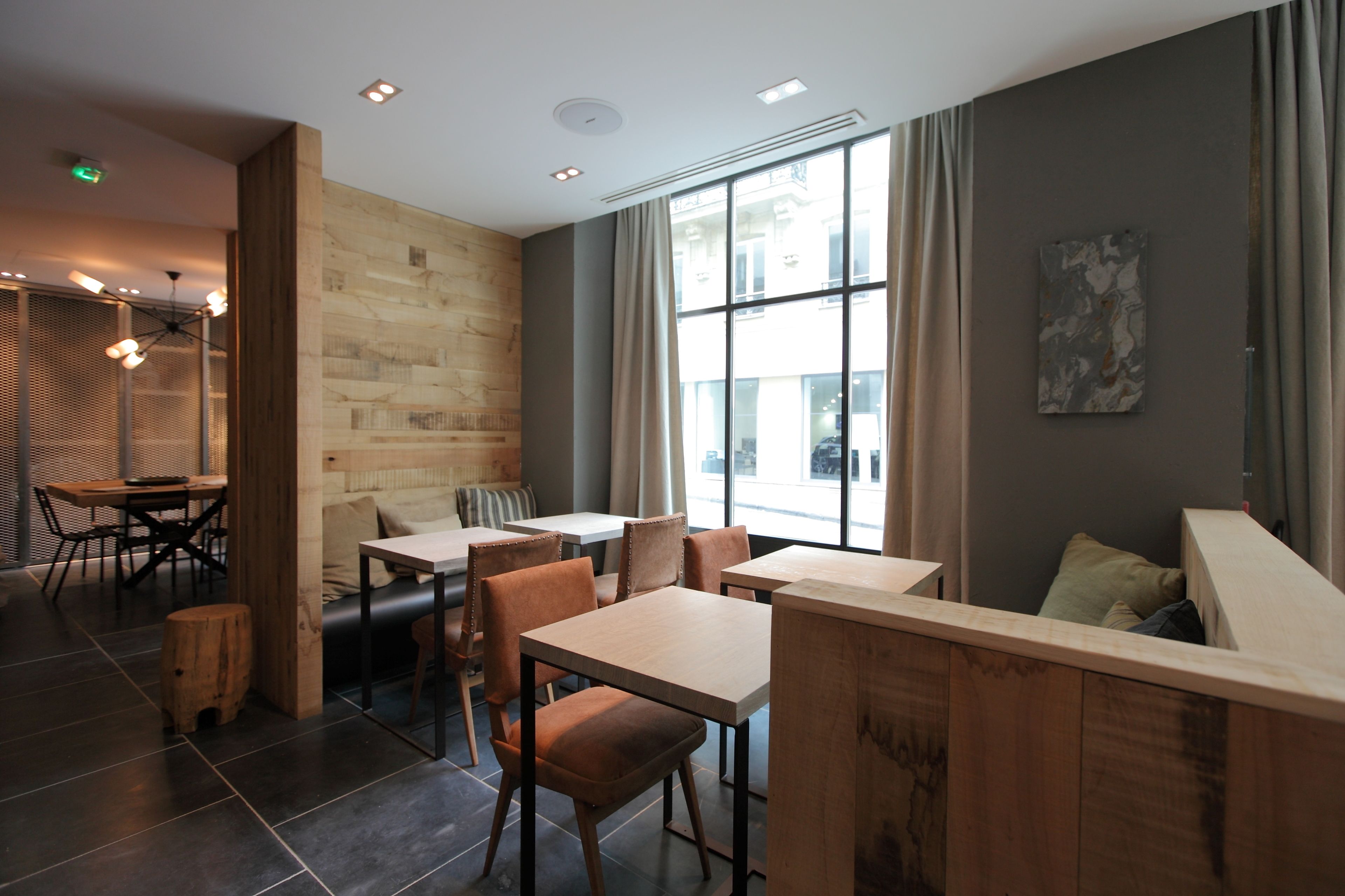 A modern cafe with wooden furniture, large windows, and a stone wall.