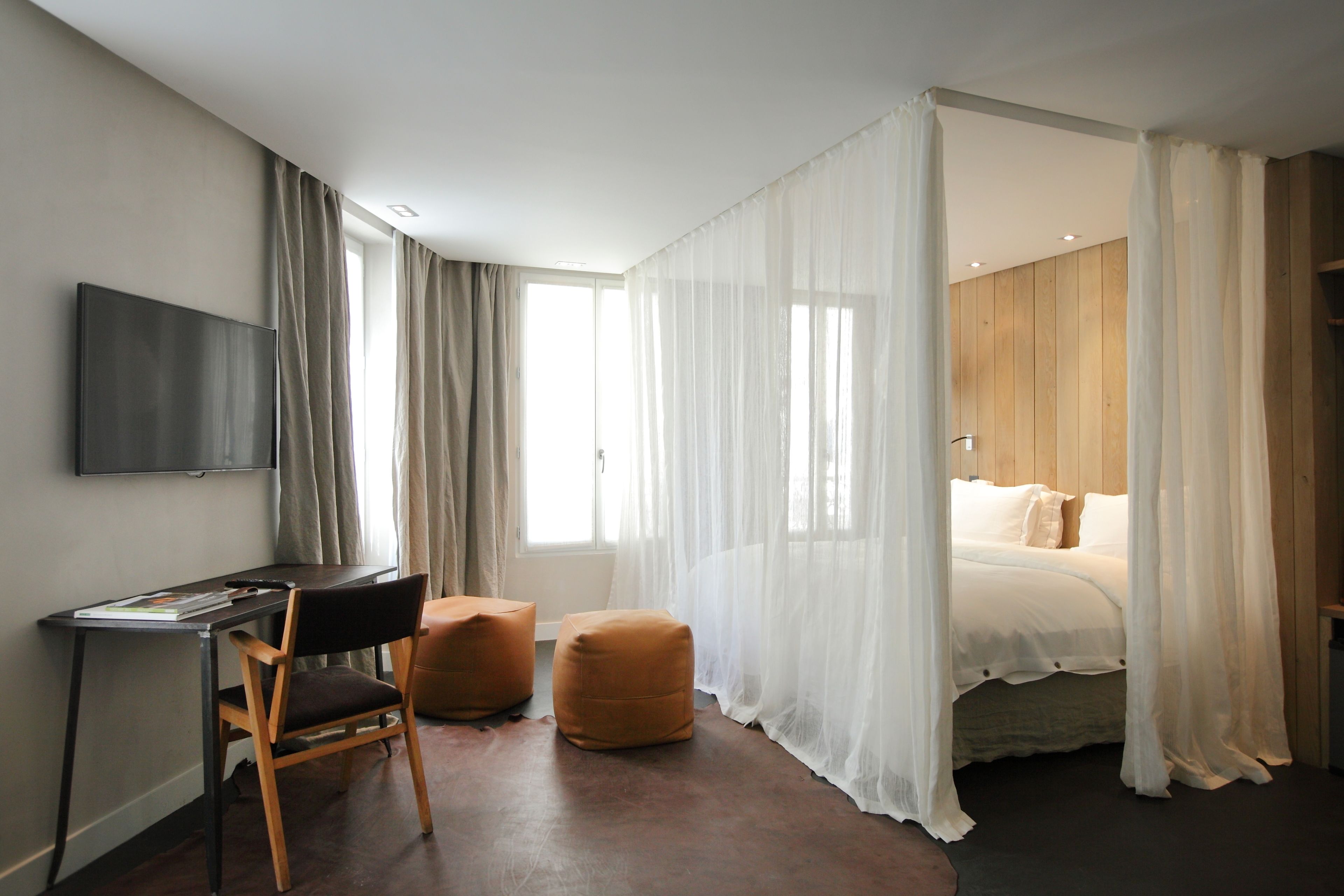 A modern hotel room with a bed, a desk, and two ottomans.