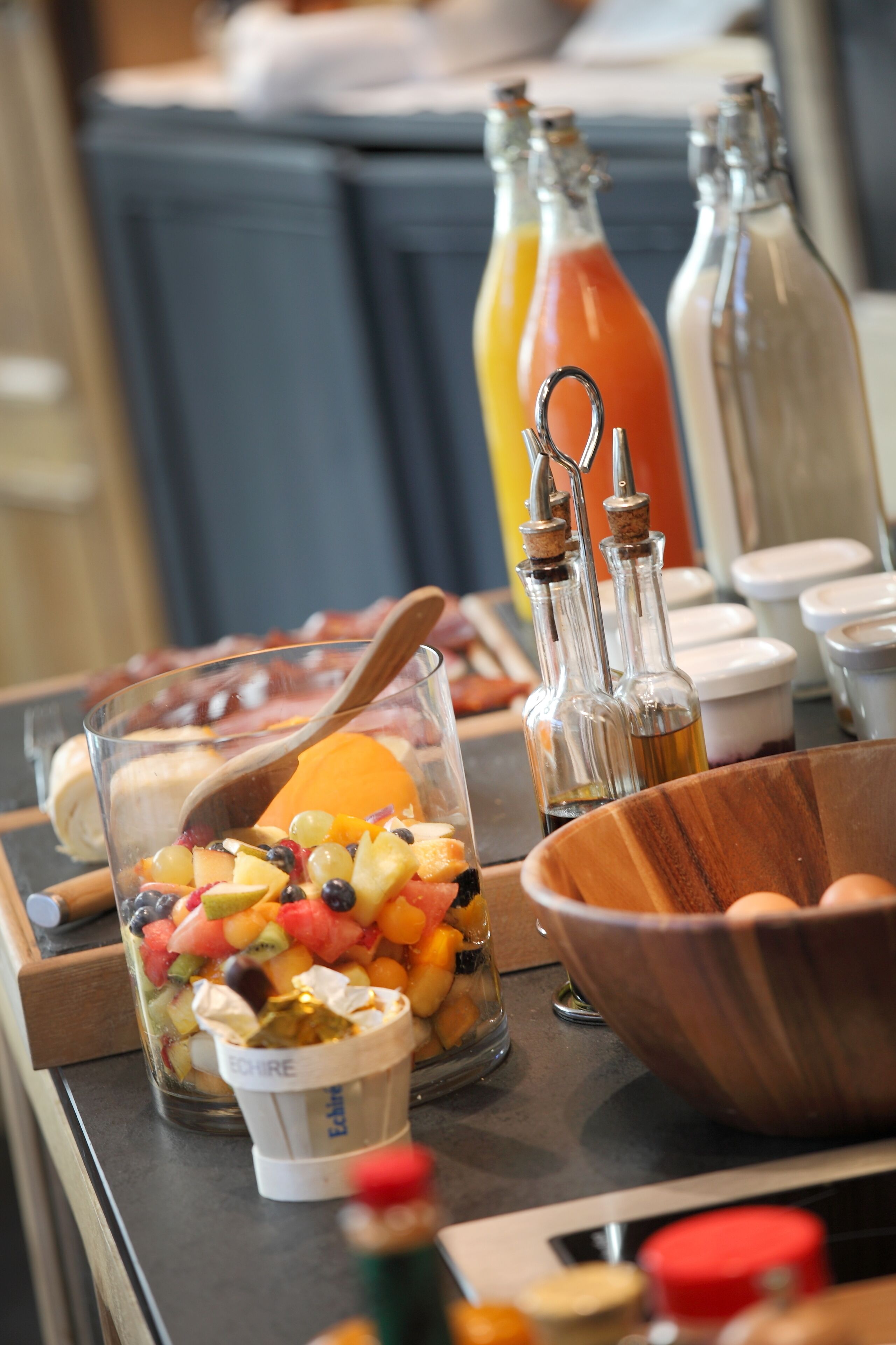 Un bufé de desayuno con una variedad de frutas, un cuenco de madera y botellas de condimentos.