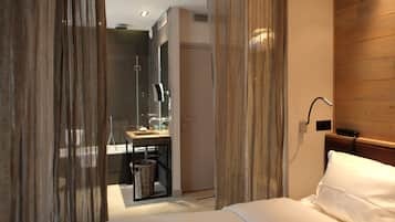 A hotel room with a bed, a desk with a sink, a mirror, and a shower area.