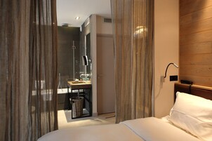 Una camera d'albergo con un letto, una scrivania con lavandino, uno specchio e un box doccia.