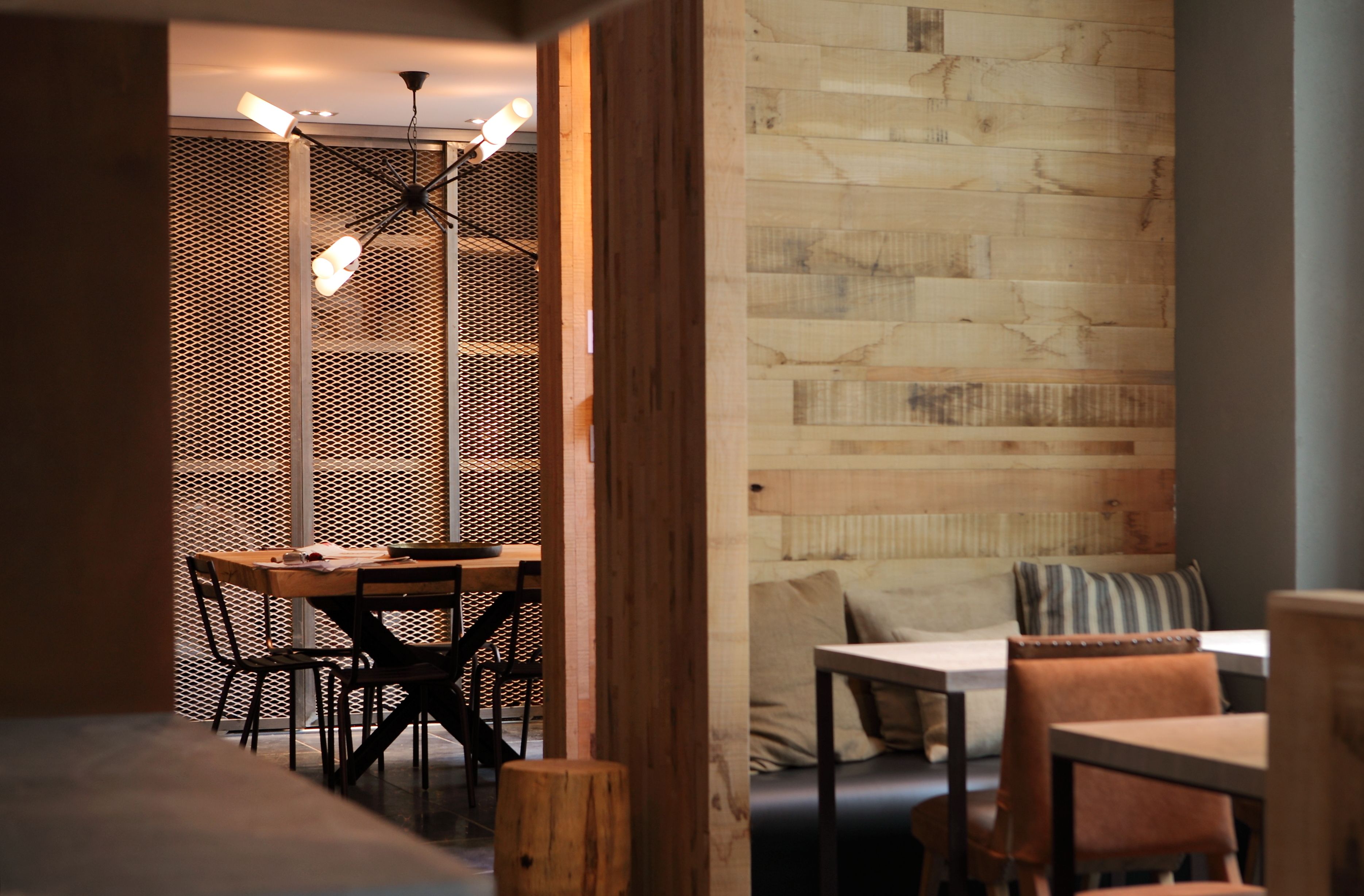 Un interior moderno con una pared de madera, una zona de comedor con mesa y sillas, y una sala de estar con banco y cojines.