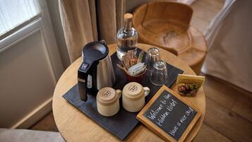 A round wooden table with a coffee maker, two mugs, a bottle of water, a small bowl, and a chalkboard sign.