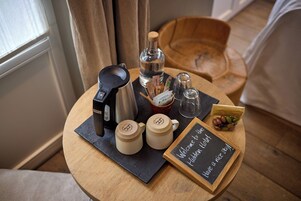 Un tavolo rotondo in legno con una macchina per il caffè, due tazze, una bottiglia d'acqua, una piccola ciotola e una lavagna.
