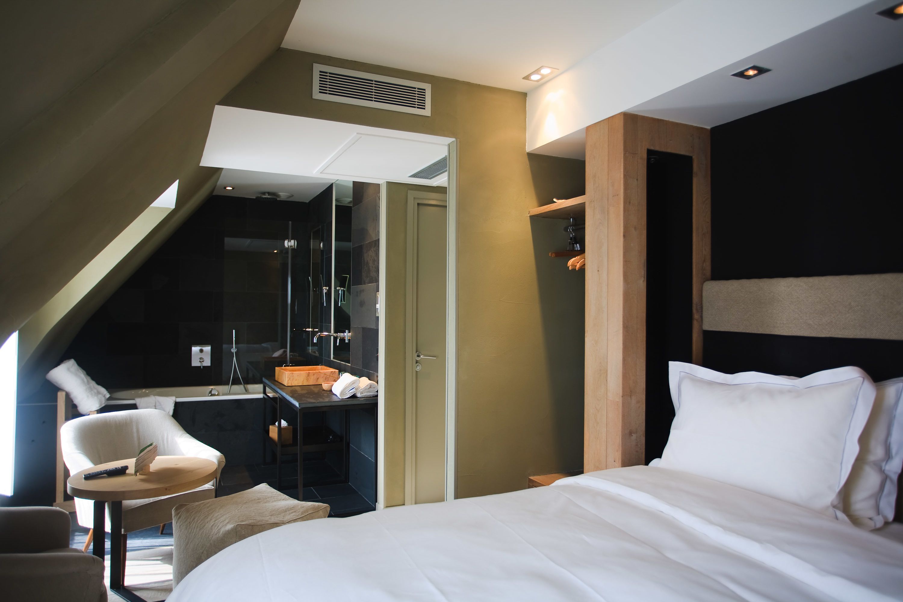 A modern hotel room with a bed, a small desk, a chair, and a shower area.