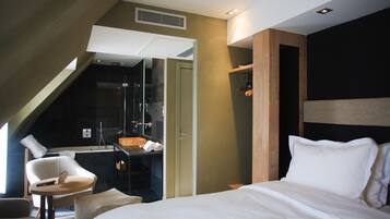 A modern hotel room with a bed, a small desk, a chair, and a shower area.
