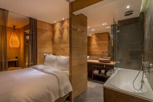 Camera d'albergo moderna con un letto grande, doccia vetrata e rivestimento murale in legno.
