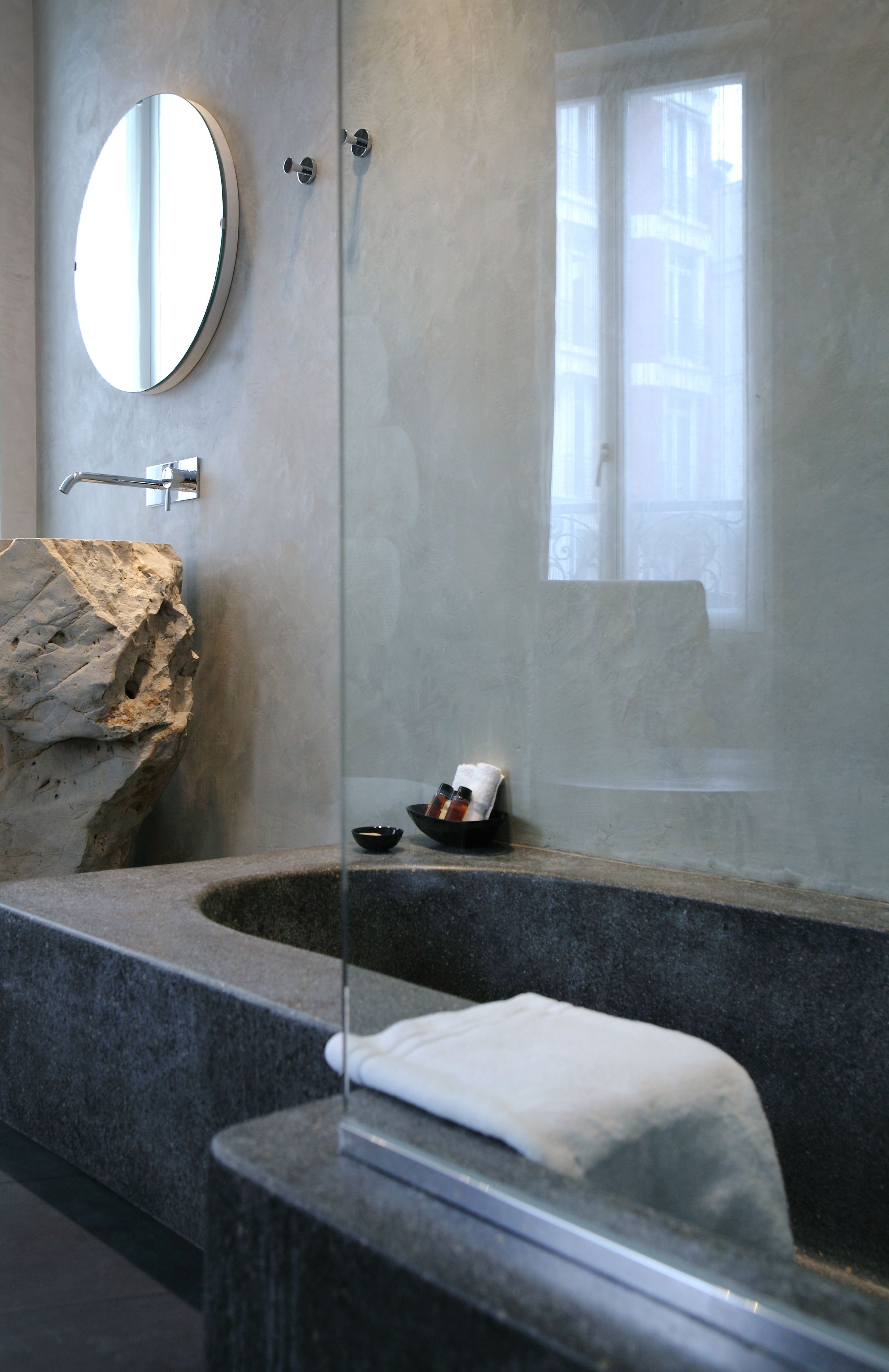 Une salle de bain moderne avec une grande baignoire, un miroir rond et un élément décoratif en pierre.