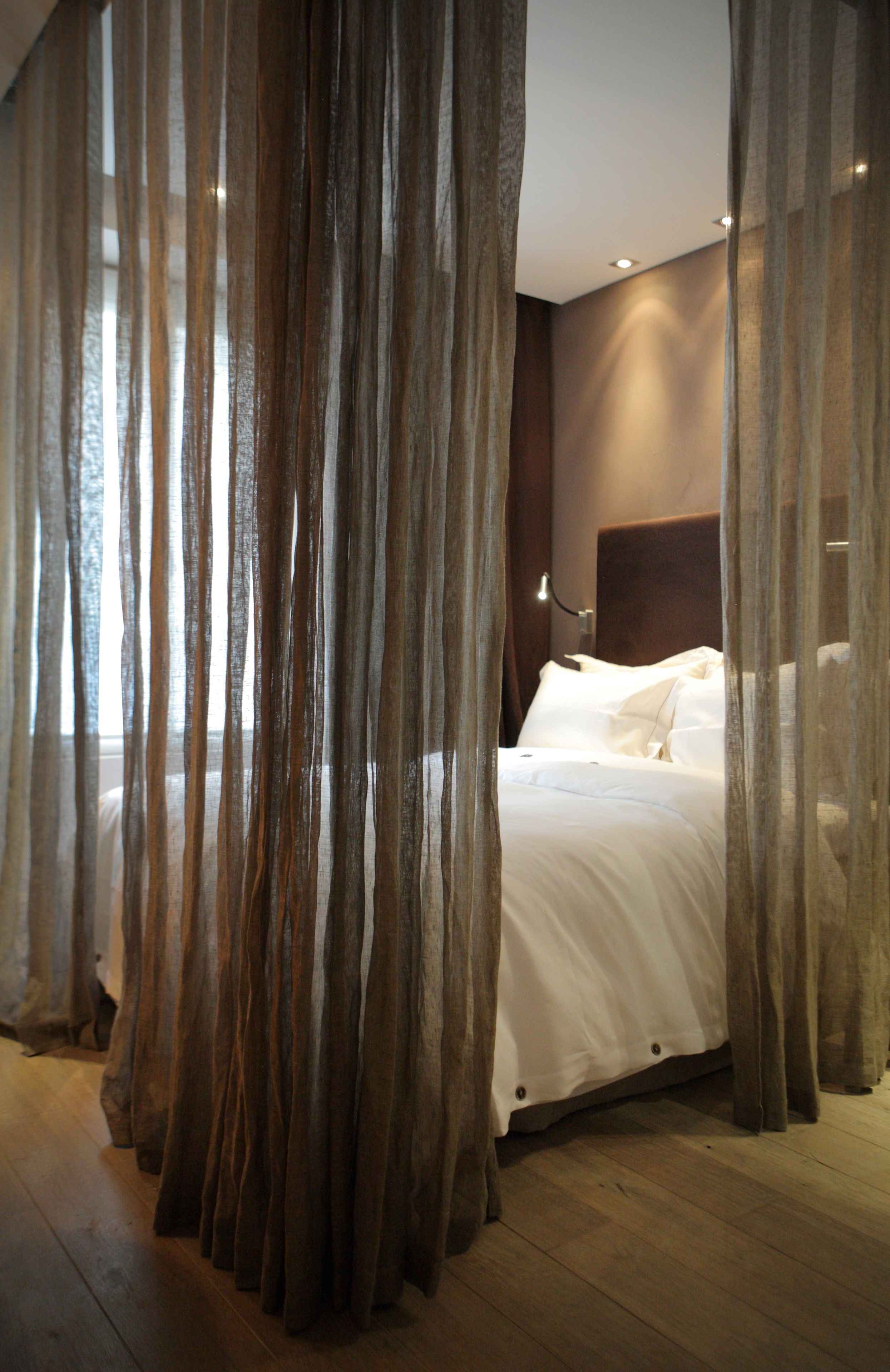 Un dormitorio con cama, cortinas, una mesita de noche y una lámpara de pared.