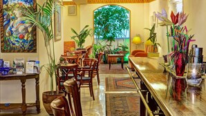 A hotel lobby with wooden chairs, a reception desk, and a large window with a view of greenery. - Nicola Hotel (Athens)