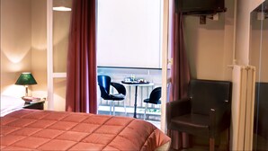 A hotel room with a bed, a TV mounted on the wall, a table with chairs outside the window, and a chair inside the room. - Nicola Hotel (Athens)