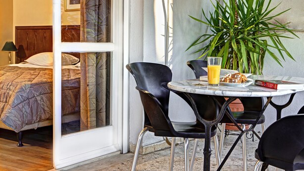 A hotel room with a bed, a dining table with chairs, a glass of orange juice, and a book. - Nicola Hotel (Athens)