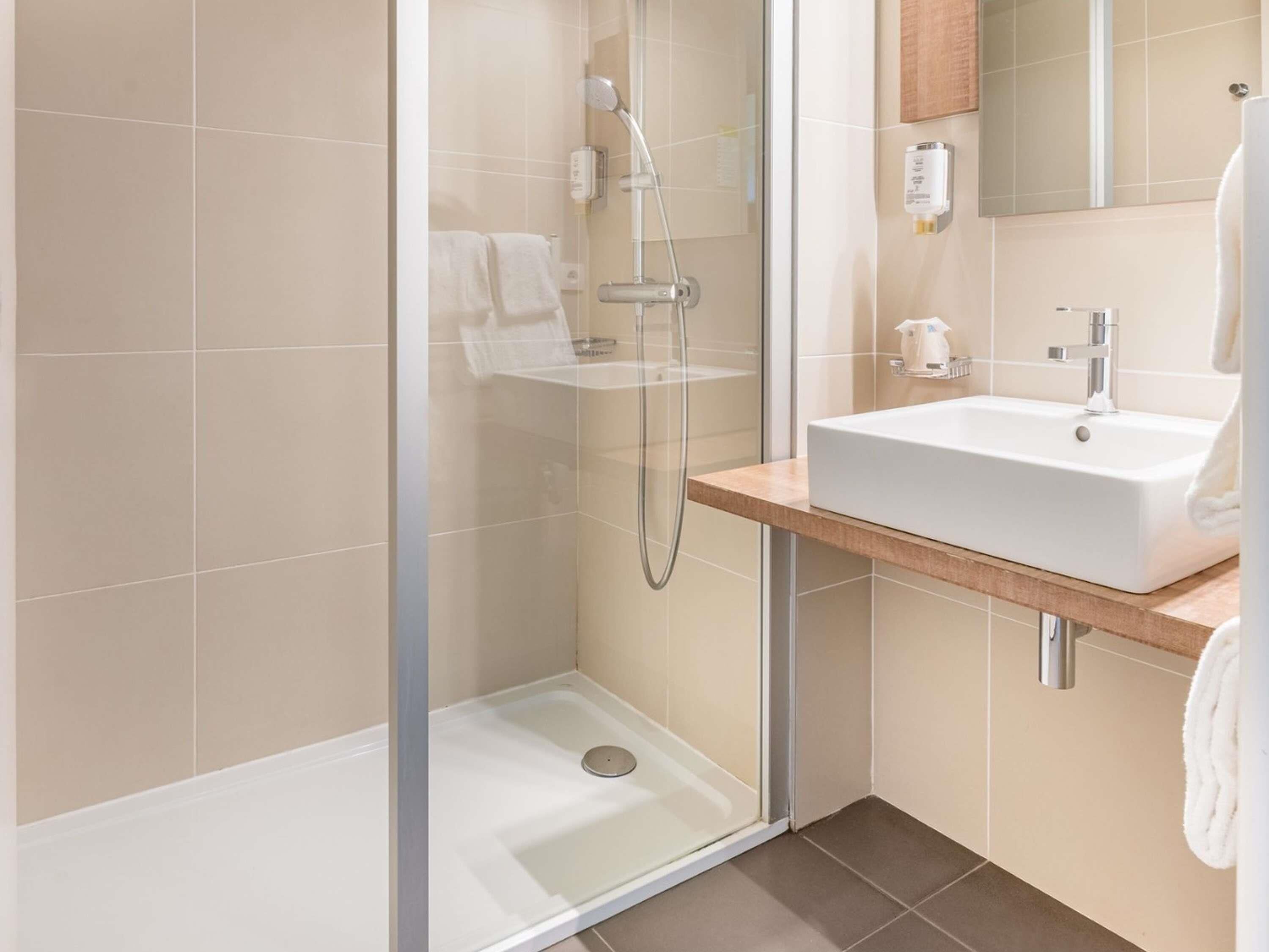 A modern bathroom with a glass-enclosed shower, a white sink, and a mirror above it.