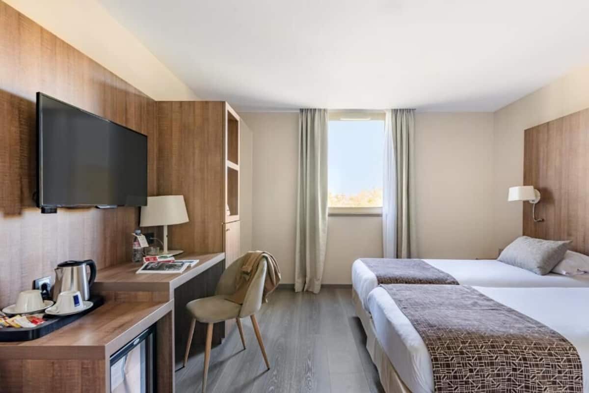 Une chambre d’hôtel équipée d’une télévision, d’un bureau, d’une chaise, de deux lits et d’une fenêtre avec des rideaux.