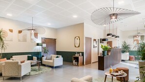 Een moderne hotel lobby met zithoeken, een receptiebalie en een plafond met een uniek geperforeerd ontwerp.