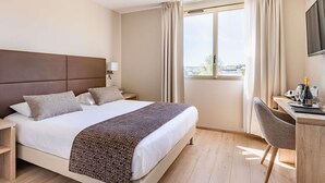 Een hotelkamer met een groot bed, een bureau met stoel, een televisie en een raam met gordijnen.