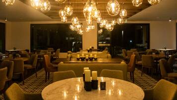 A restaurant with round tables, candle centerpieces, and hanging spherical chandeliers.