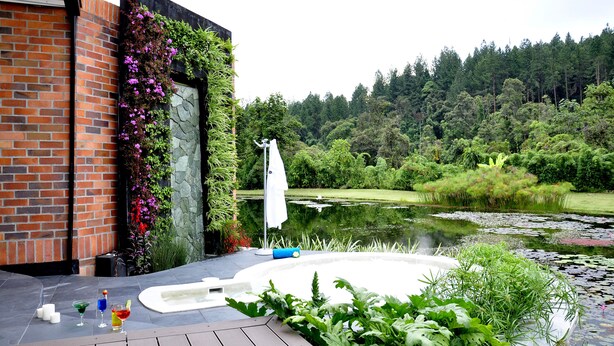 Um edifício moderno com fachada de tijolo, porta de vidro e área de jardim com lago e plantas.
