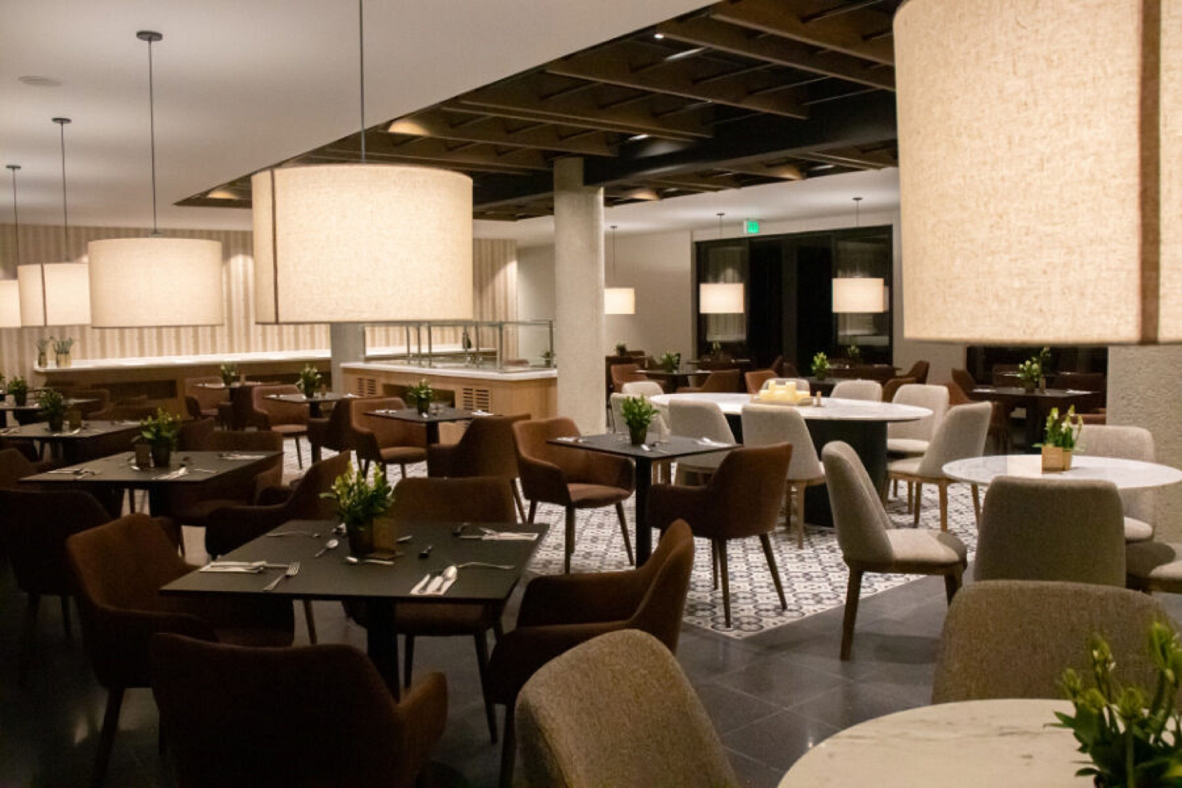 Un restaurant spacieux doté de plusieurs espaces de restauration, notamment des tables rondes et des banquettes, ainsi qu’un bar avec des tabourets.