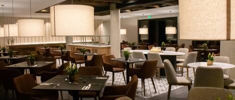 A spacious restaurant with multiple dining areas, including round tables and booths, and a bar area with stools.