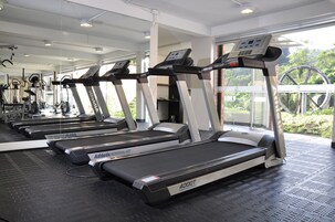 Un gimnasio con cintas de correr, un espejo grande y ventanas amplias que dan a zonas verdes.