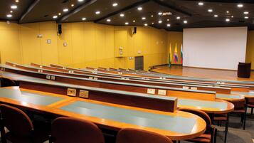A lecture hall with rows of seating, a stage, and a projector screen.