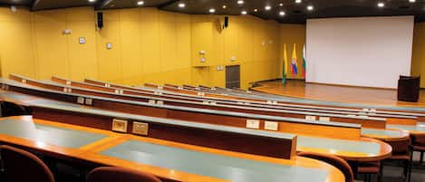 Un auditorio con filas de asientos, un escenario y una pantalla proyectora.