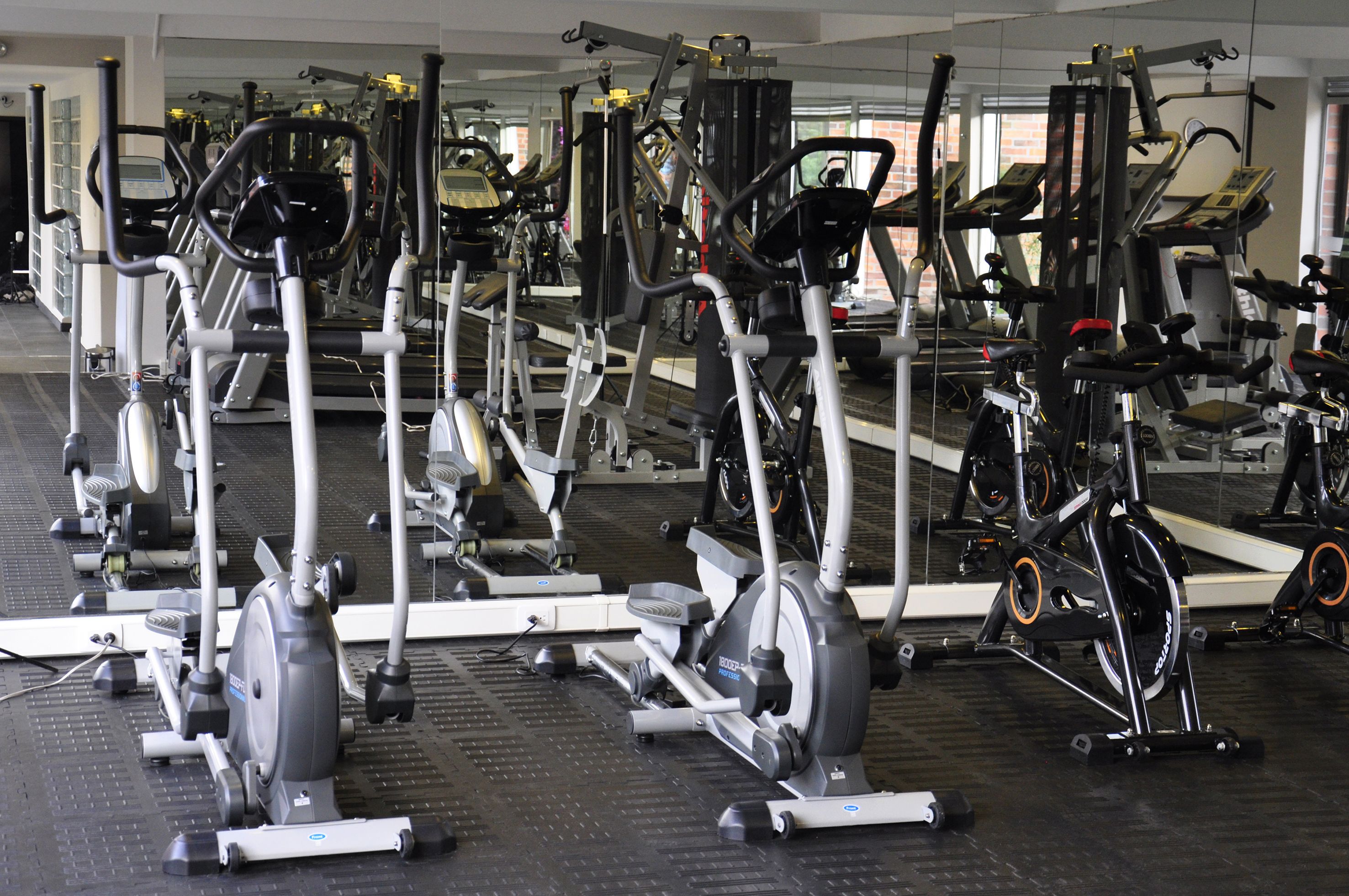 Et fitnesscenter med diverse træningsmaskiner, herunder løbebånd og spinningcykler, opstillet i rækker.