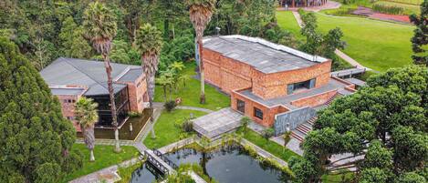 A modern building with a brick facade, a glass structure, and a surrounding garden with a pond.