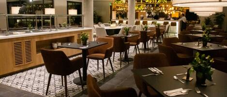 A restaurant with a bar area, multiple tables and chairs, and a buffet counter.