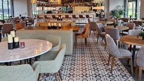 Um restaurante com mesas e cadeiras redondas, chão estampado e luminárias pendentes.