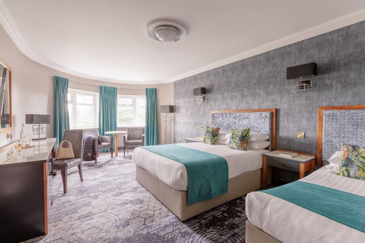 A hotel room with two beds, a desk, a chair, a small table, and a large window with curtains.
