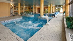 Una piscina interior con fuente, rodeada de columnas y plantas en macetas.