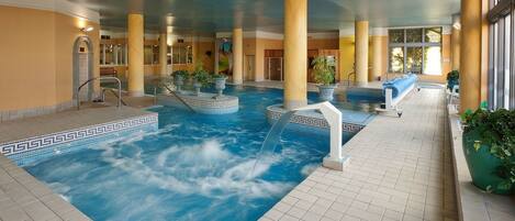 Una piscina interior con fuente, rodeada de columnas y plantas en macetas.