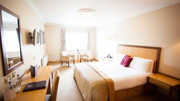 A hotel room with a bed, bedside table, desk, chair, and a small table with a lamp.