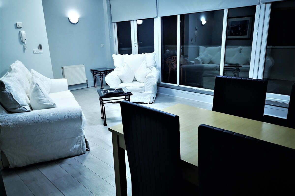 A modern living room with a sofa set, a dining table, and chairs. There is a small side table and a radiator.