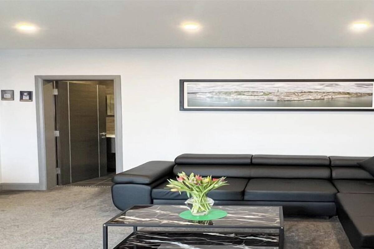 A modern living room with a black sectional sofa, a marble coffee table, and a framed landscape painting on the wall.