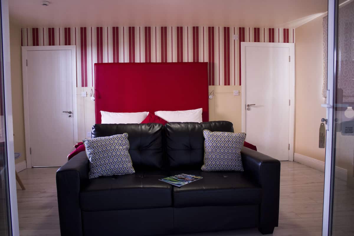 A bedroom with a black leather sofa, a red headboard, and striped wallpaper.