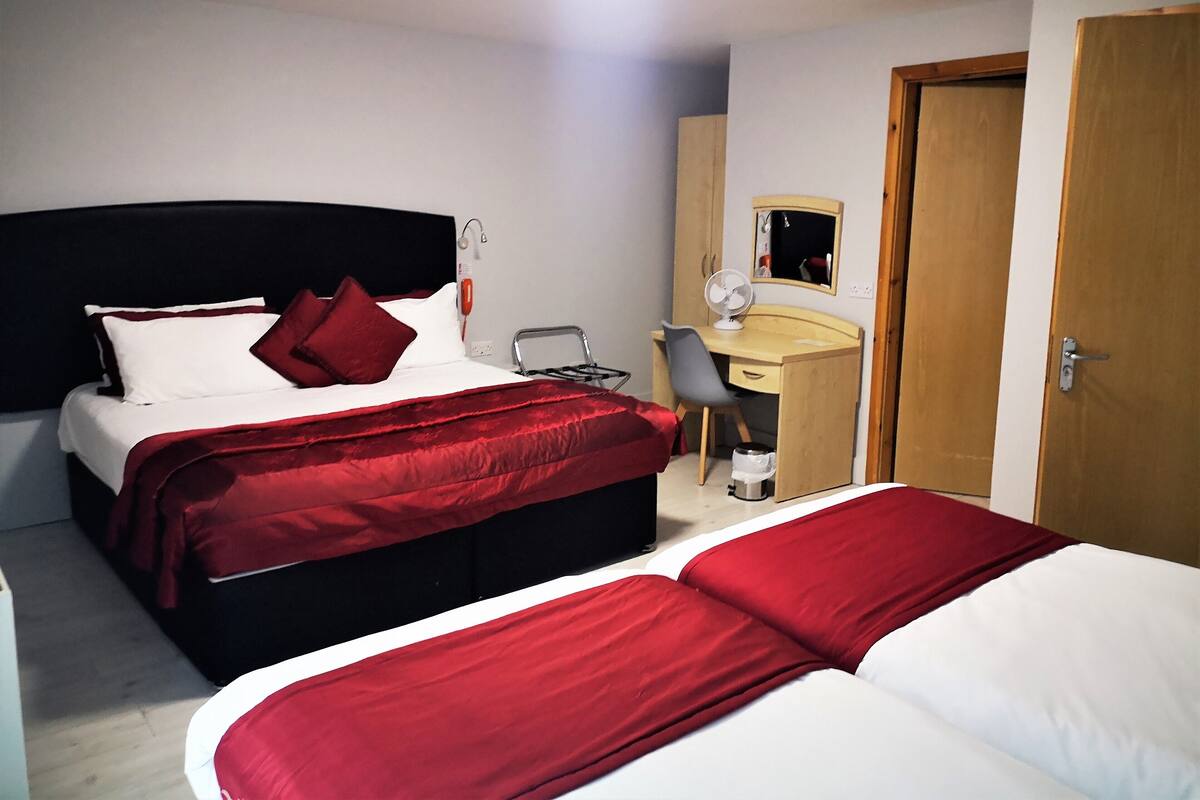 A hotel room with two beds, a desk, a chair, a mirror, and a door.