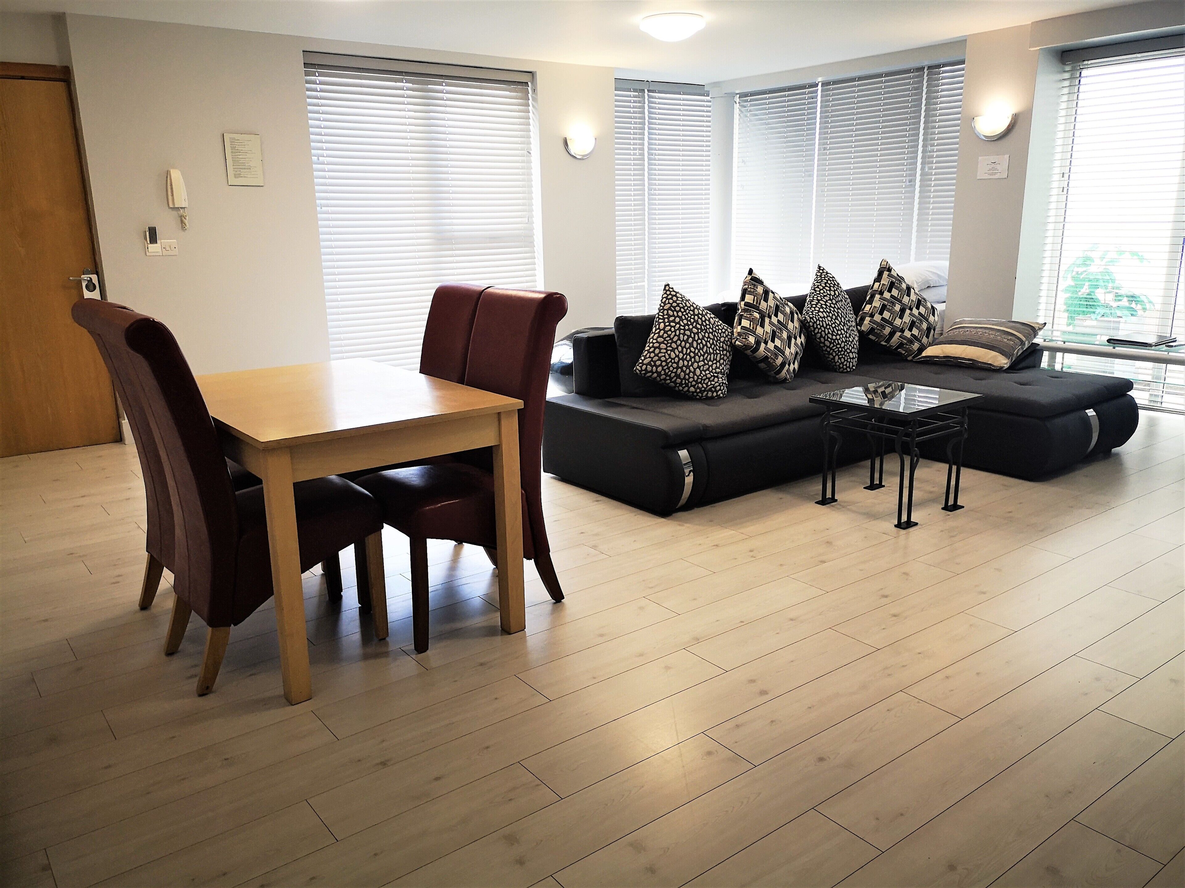 A living room with a wooden dining table, dark brown chairs, a black sofa with patterned cushions, and a small black coffee table.