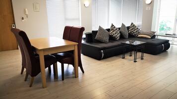 A living room with a wooden dining table, dark brown chairs, a black sofa with patterned cushions, and a small black coffee table.