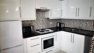 Una cocina con armarios blancos, encimera negra, estufa, horno y lavaplatos.
