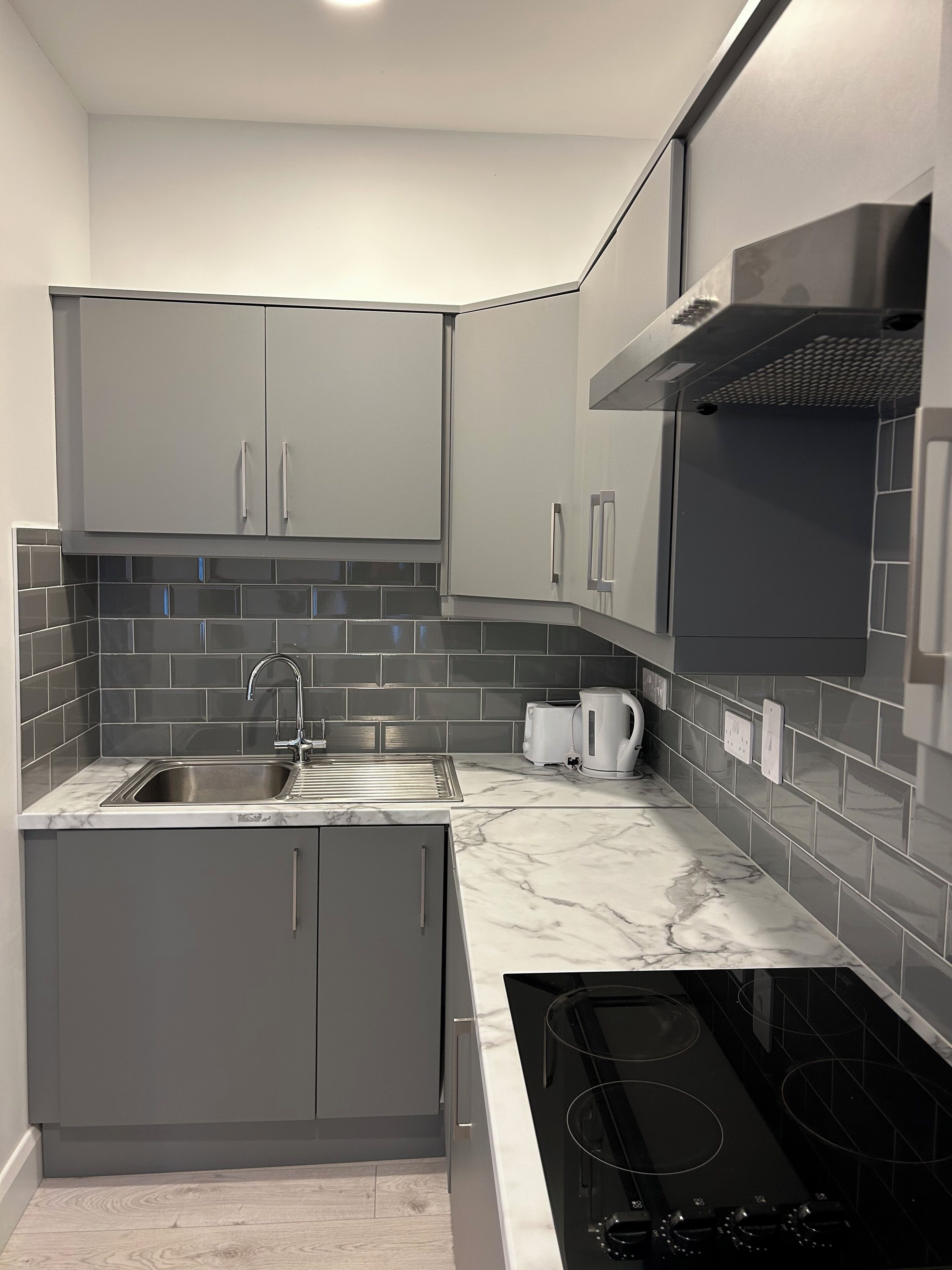 A modern kitchen with grey cabinets, a stainless steel sink, a black stove, and a tiled backsplash.