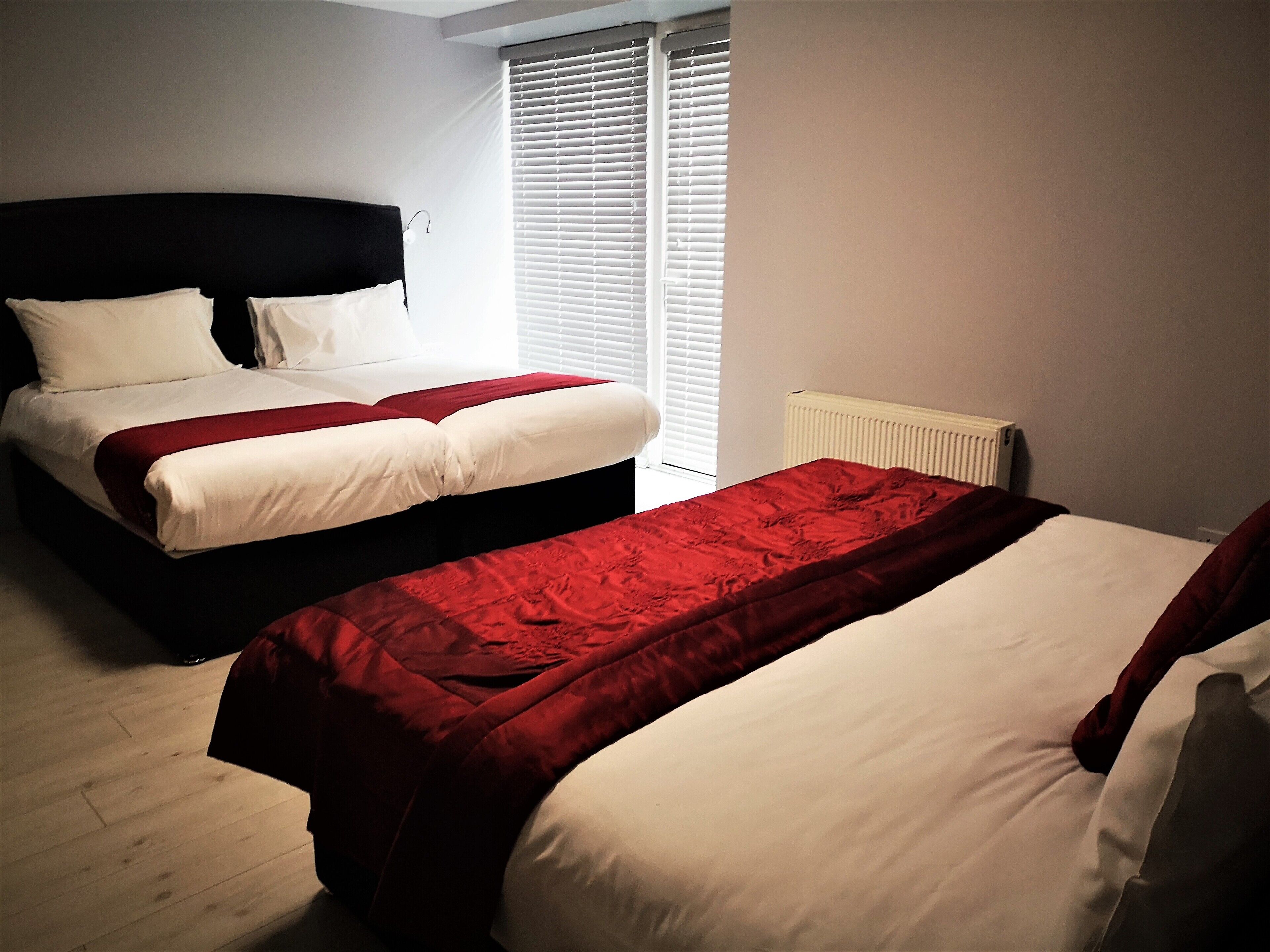 A hotel room with two beds, a radiator, and a window with blinds.