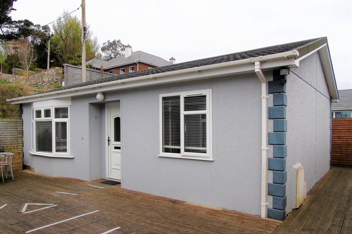 A single-story building with a grey exterior, white window frames, and a small front door.