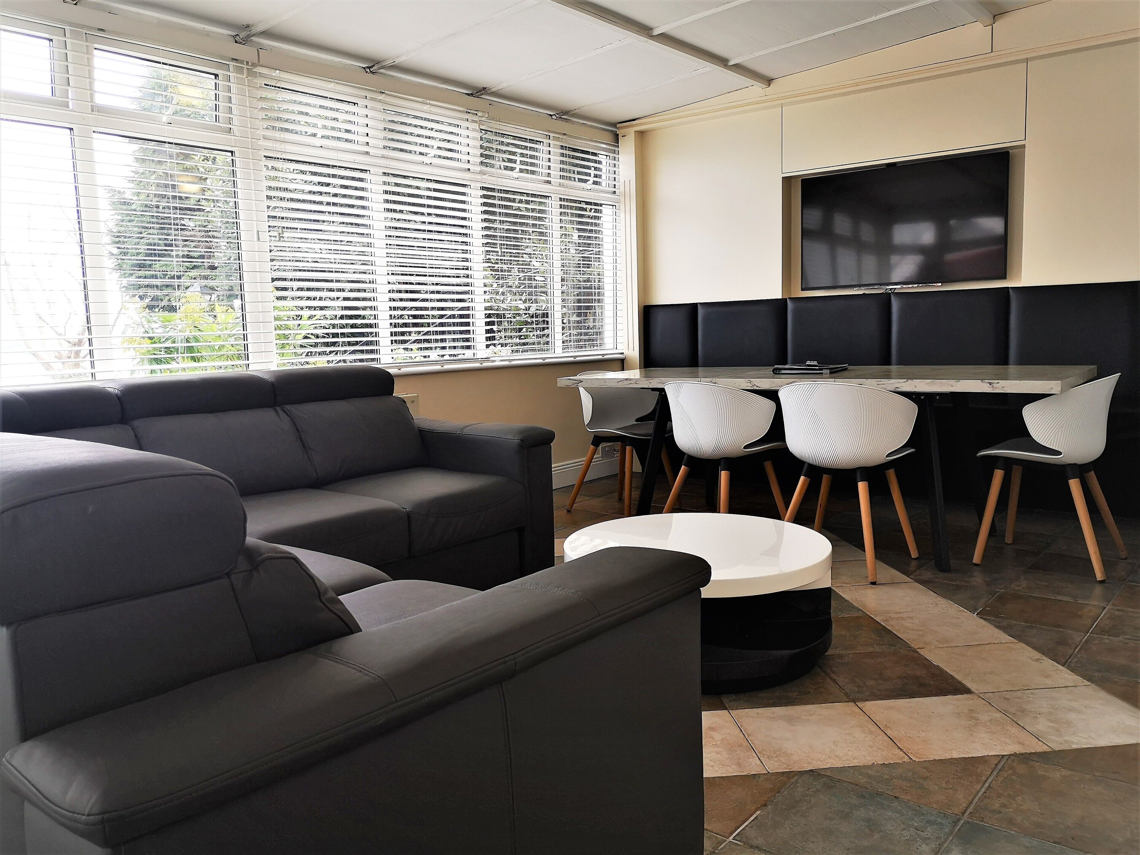 A modern living room with a sofa, a dining table with chairs, and a TV mounted on the wall.